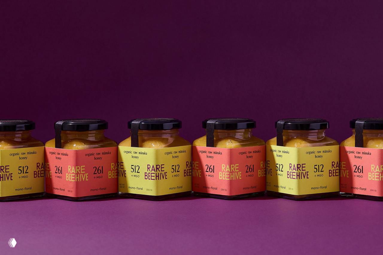 Ряд баночек Rare Beehive на пурпурном фоне, выстроенные в линию; повторяющийся мотив этикеток подчёркивает фирменную систему упаковки.