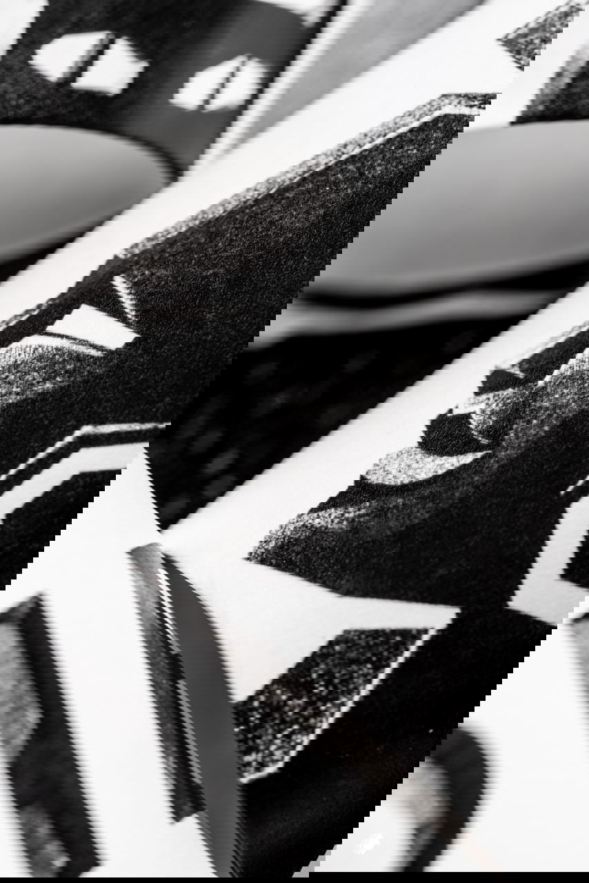 Макро‑съёмка линогравюры на бумажном стаканчике: зернистая текстура печати и геометрический профиль лица в чёрно‑белой графике.