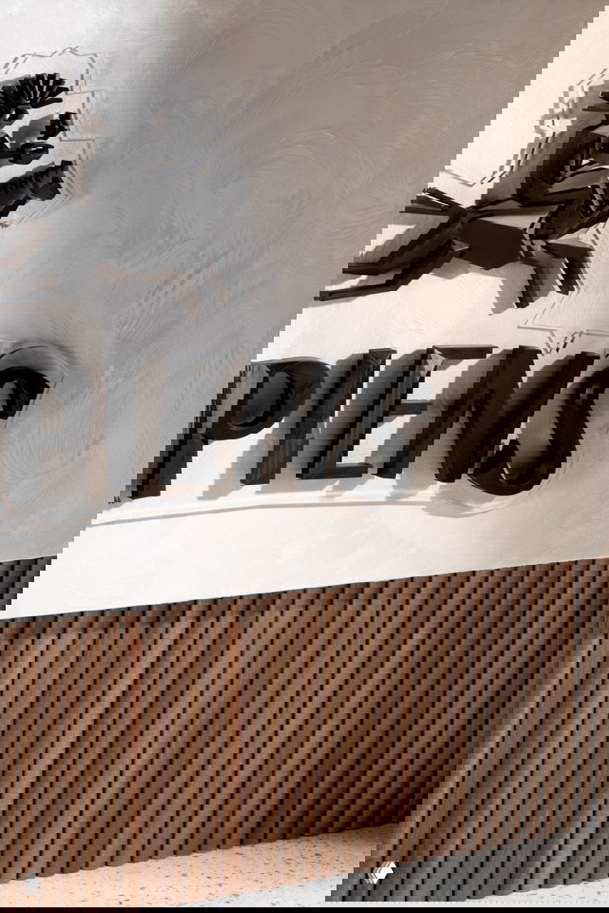 Крупный план интерьерной вывески: объёмные чёрные буквы SAPIENS на фактурной светлой стене и декоративная деревянная облицовка внизу.