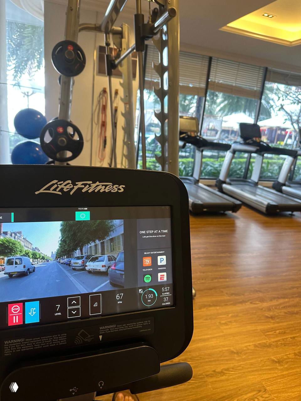 Интерьер тренажёрного зала с тренажёрами LifeFitness, вид на беговые дорожки и большие окна, дневной свет и город за окном