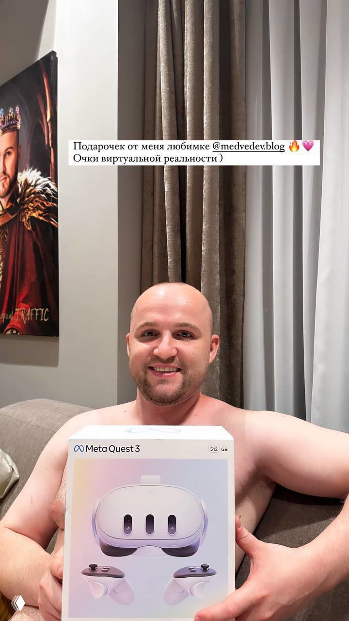 Улыбающийся мужчина на диване держит коробку Meta Quest 3; видна подпись о подарке от блогера, интерьер комнаты на заднем плане.