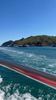 Вид с моторной лодки на бирюзовое море и берег Нячанга, след от лодки на воде и холмы вдали под чистым небом