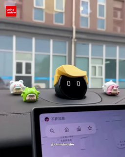 Крупный план мини‑робота на панели автомобиля, дизайн с выразительными глазами и декоративными фигурками вокруг, кадр сбоку на городской фон.