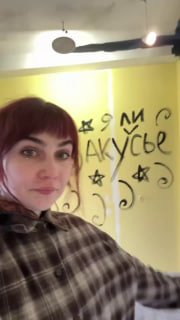 Женщина в помещении кофейни на фоне стены с граффити; кадр подчёркивает интерьер и атмосферу кукольного театра‑кафе.