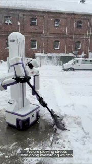 Робот-уборщик Reflex Robotics на заснеженной улице у кирпичного здания в Нью-Йорке, очищает тротуар и сбрасывает снег.
