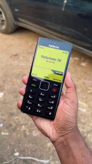 Рука держит телефон с интерфейсом в стиле Nokia 1280: монохромный экран, имя оператора и крупные физические кнопки на переднем плане.