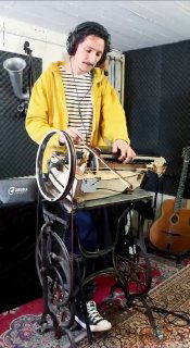 Музыкант в жёлтой толстовке управляет швейной лирой-экспериментом; заметны гитара на фоне и элементы терменвокса.