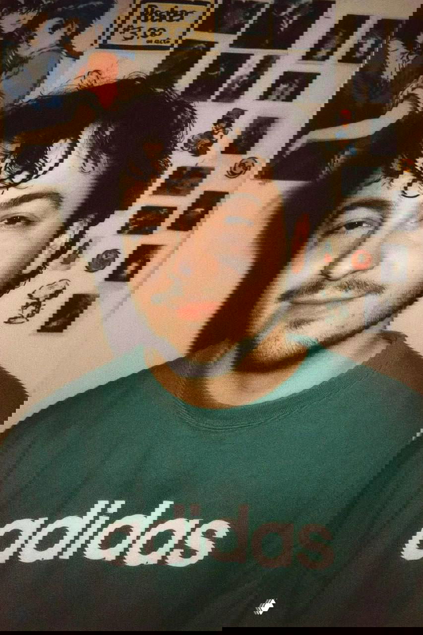 Портрет мужчины в зеленом свитшоте Adidas на фоне коллажа из постеров и наклеек, зернистая мыльничная текстура и ретро‑освещение.