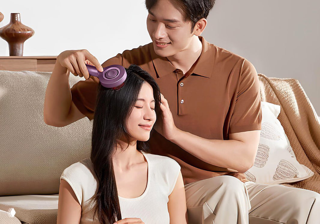 Мужчина массажирует женщину массажно-расчёской Xiaomi на диване: уютная сцена, демонстрация использования устройства в паре.