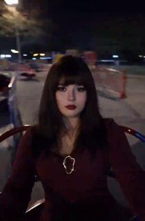 Ночная сцена: подросток или взрослый в образе с серьёзным лицом на карусели, волосы слегка развеваются, фон парка размыт.