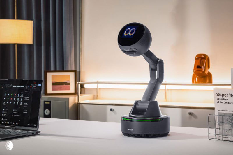 Робот-компаньон Lenovo на рабочем столе: гибкий штатив с круглой головой, база с подсветкой, ноутбук и предметы офиса на заднем плане