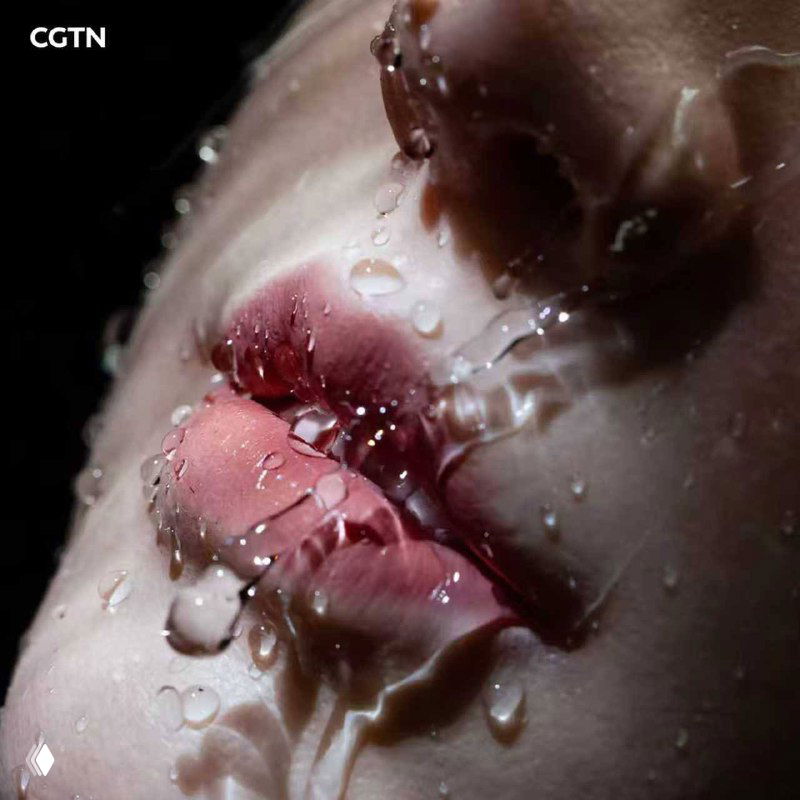 Макрофото губ и капель воды на поверхности кожи роботизированного лица, подчёркивающее реализм текстуры и материалов.