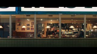 Ночной кадр витрины закусочной или кафе: через окно видно интерьер зала и расставленные столы — сцена из рекламного фрагмента ролика.