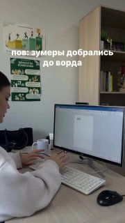 Человек за компьютером редактирует документ Word на мониторе; видны клавиатура, мышь и учебные плакаты на стене, рабочая обстановка.