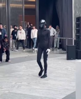 Андроид IRON от Xpeng в черном костюме шагает по подиуму, демонстрируя модельную походку; на фоне — зрители.