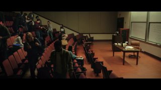 Кадр лекционной аудитории: преподаватель у доски и расставленные ряды кресел, передний план с аудиторией — сцена из рекламного сюжета.