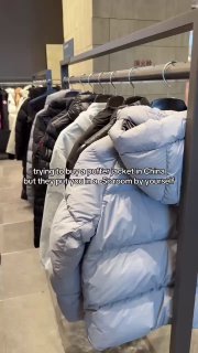 Ряд пуховиков на вешалке в магазине на фоне входа в холодовую комнату для проверки теплоизоляции изделий.