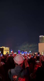 Толпа людей с поднятыми телефонами наблюдает за дрон-шоу в Лас-Вегасе; вдалеке в небе видны точечные световые фигуры дронов.