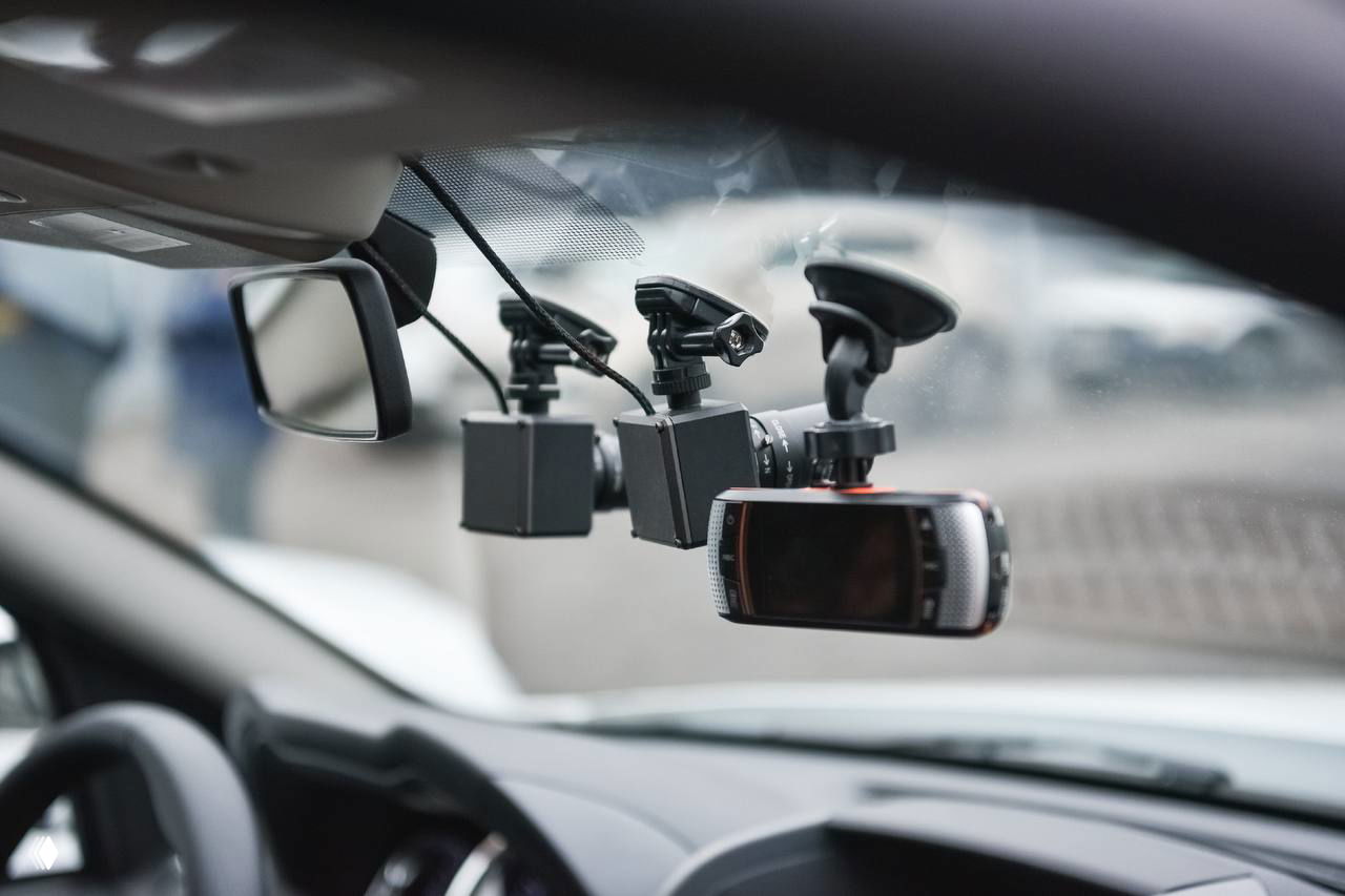 Несколько регистраторов и камеры, закреплённые на лобовом стекле автомобиля, иллюстрация мобильного видеоконтроля для фиксации нарушений во дворах и у контейнерных площадок.