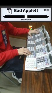 Кадр в вертикальном формате: исполнитель играет на ряду калькуляторов, на столе рядом лежит кубик Рубика и другие мелкие предметы.