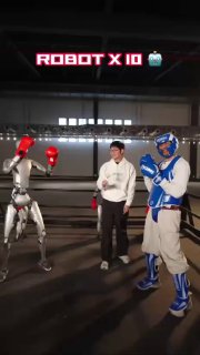 На фото сцена роботобоя: два робота в боксерских перчатках и человек в повседневной одежде на ринге, подготовка к поединку.