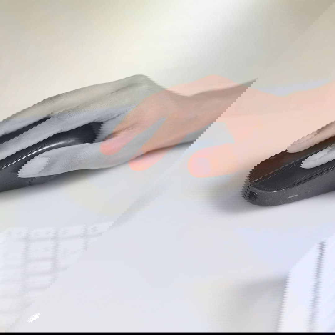 Фото руки, управляющей мышью Phase, показывающее размер устройства в руке и его использование в режиме мыши на столе с клавиатурой.