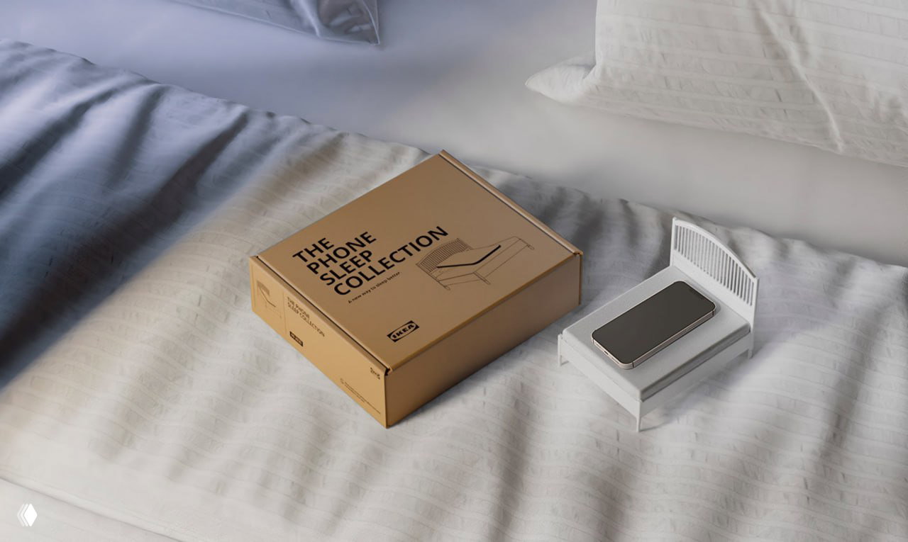 Мини-кроватка и упаковочная коробка «The Phone Sleep Collection» на кровати, телефон лежит в кроватке — рекламный ракурс продукта IKEA.