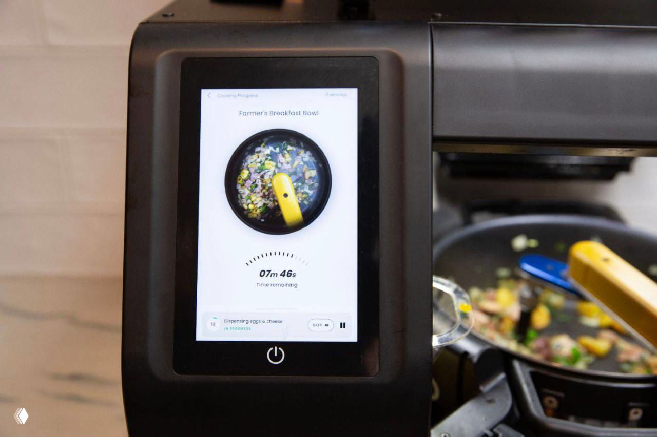 Крупный план сенсорного дисплея Posha с интерфейсом рецепта и таймером; внизу видна рабочая сковорода в процессе готовки.