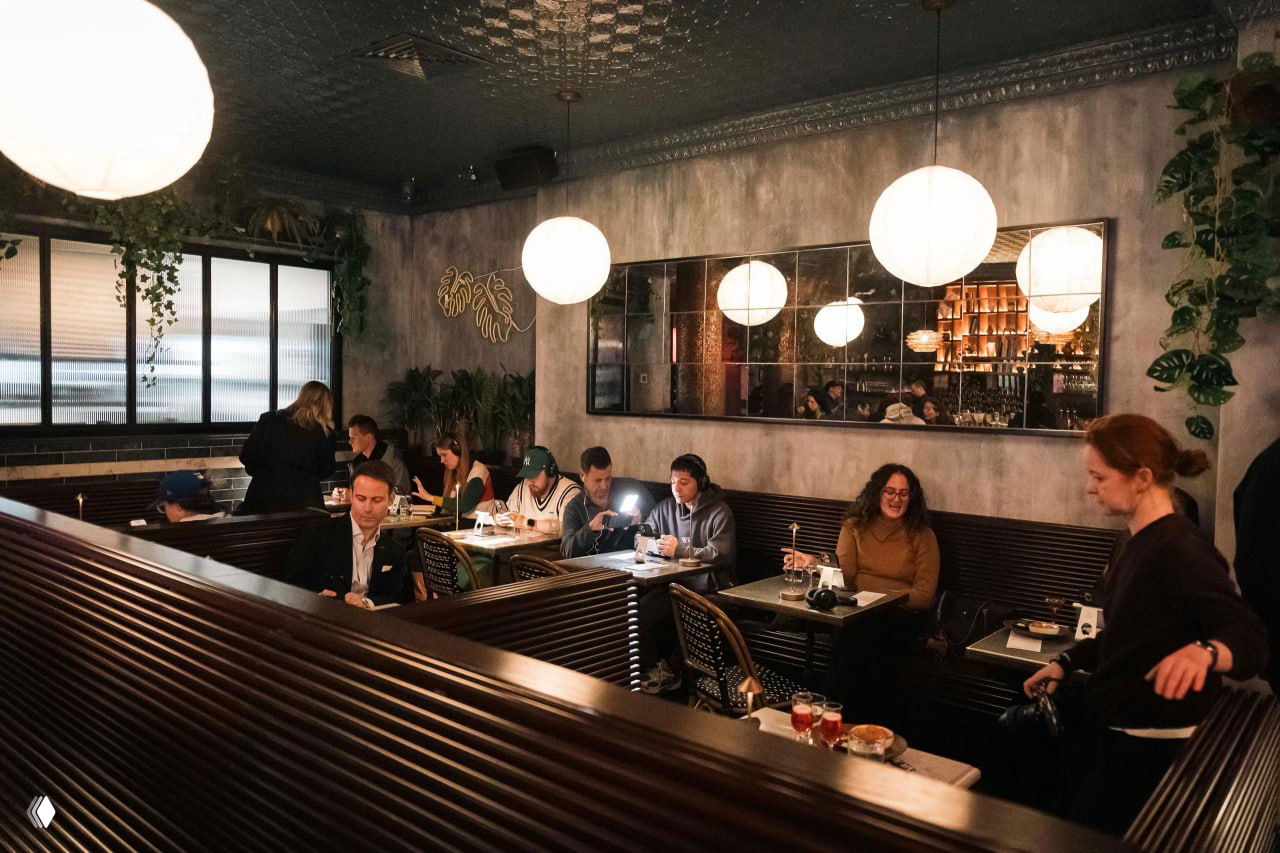 Интерьер кафе с отдельными кабинами и столиками на одного: посетители сидят поодиночке с телефонами на подставках и наушниками.