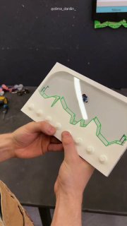 Руки держат белую игрушку-акватубик с зелёной трассой и миниатюрным мотоциклистом — версия Gravity Defied