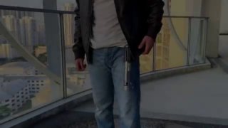 Человек держит самодельный «джедайский меч» на балконе: видна рукоять, прозрачная пружинящая трубка и светящаяся LED-лента, кадр из ролика.