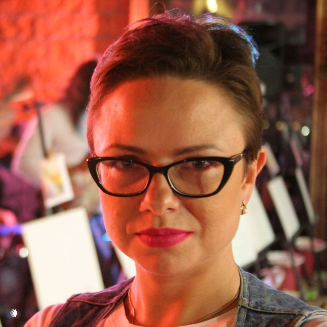 Портрет женщины в очках, короткие волосы и лёгкий макияж, нейтральный фон — спокойный крупный план лица и взгляда в камеру.