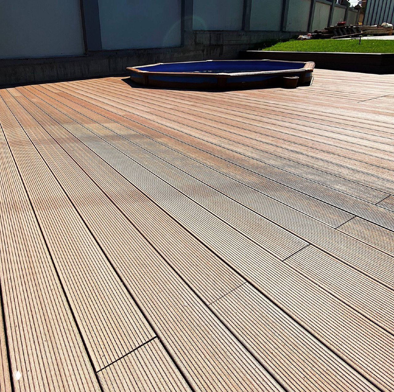 Крупный план рифлёной поверхности композитного настила (ДПК) — аккуратная укладка планок и вид на небольшой бассейн на заднем плане.