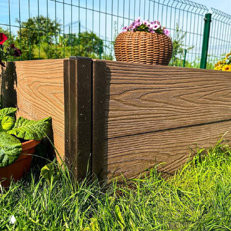 Пустая сборная грядка из композитного ДПК с чёрной плодородной почвой внутри; вокруг — зелёная трава и декоративные горшки с цветами.