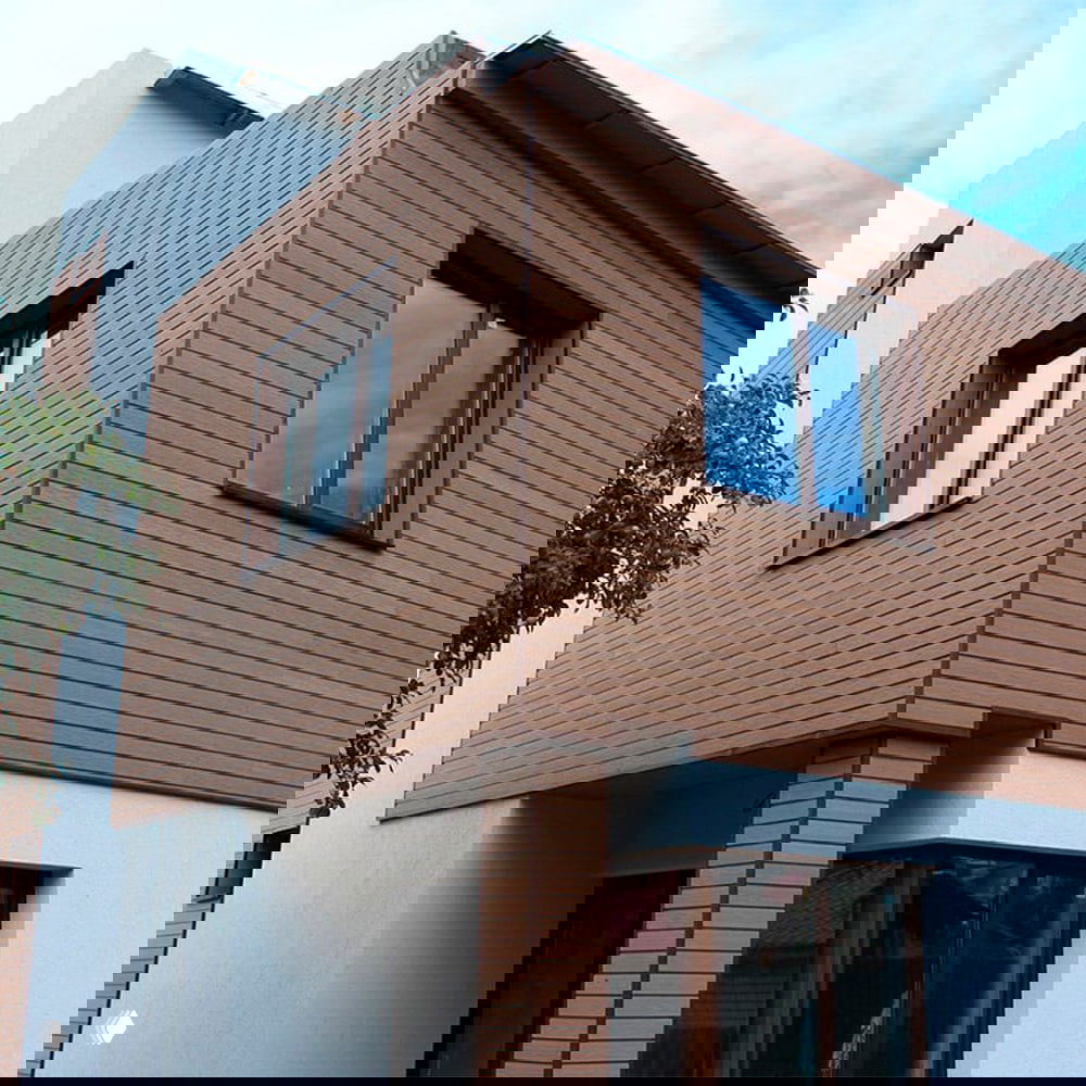 Фасад дома, обшитый панелями ДПК: ровные горизонтальные планки композитного материала коричневого оттенка на внешней стене здания.