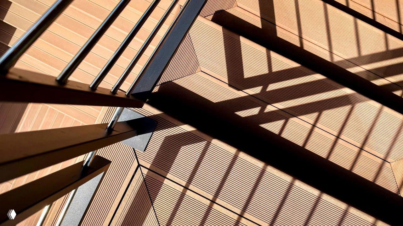 Крупный план ступеней и рельсов ограждения над настилом ДПК: рифлёная текстура досок, геометричные тени и детали монтажа.