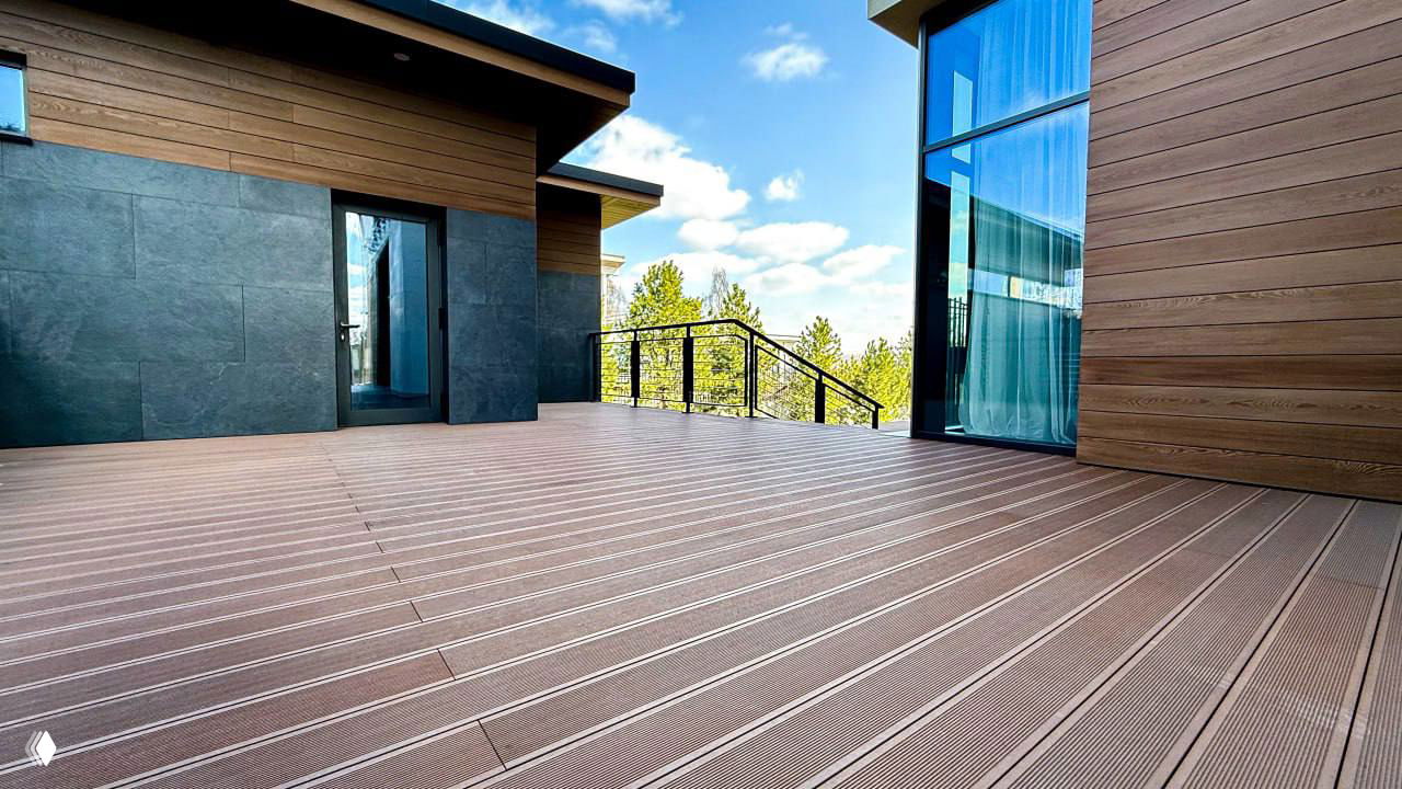 Панорамный план большого патио из ДПК: ровные ряды композитных досок с видимыми стыками и фасадами современного дома на заднем плане.