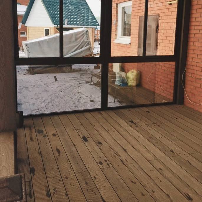 Вид изнутри на ДПК настил террасы и большие стеклянные панели; заметен снег и кирпичная стена дома — монтаж в холодный период.