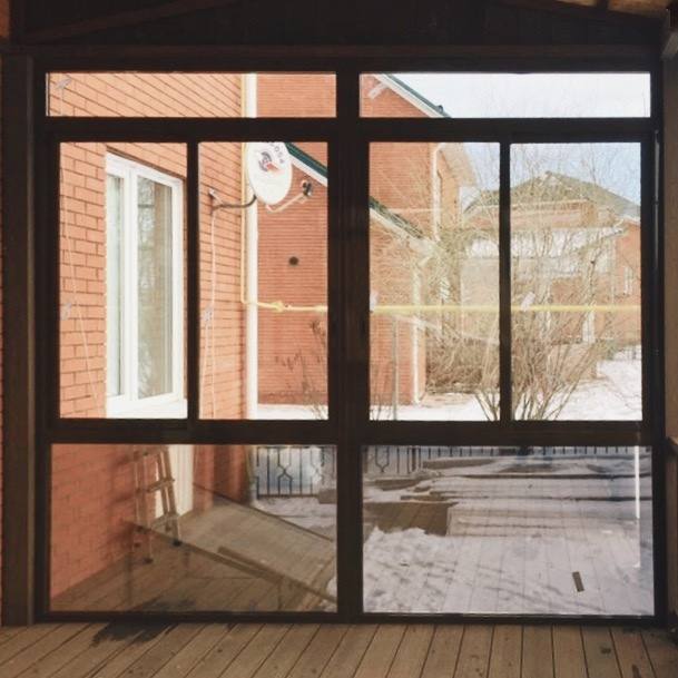 Окна террасы и металлический каркас; через стекла виден двор и кирпичный дом, пример зимнего исполнения проекта в частном секторе Кемерово.