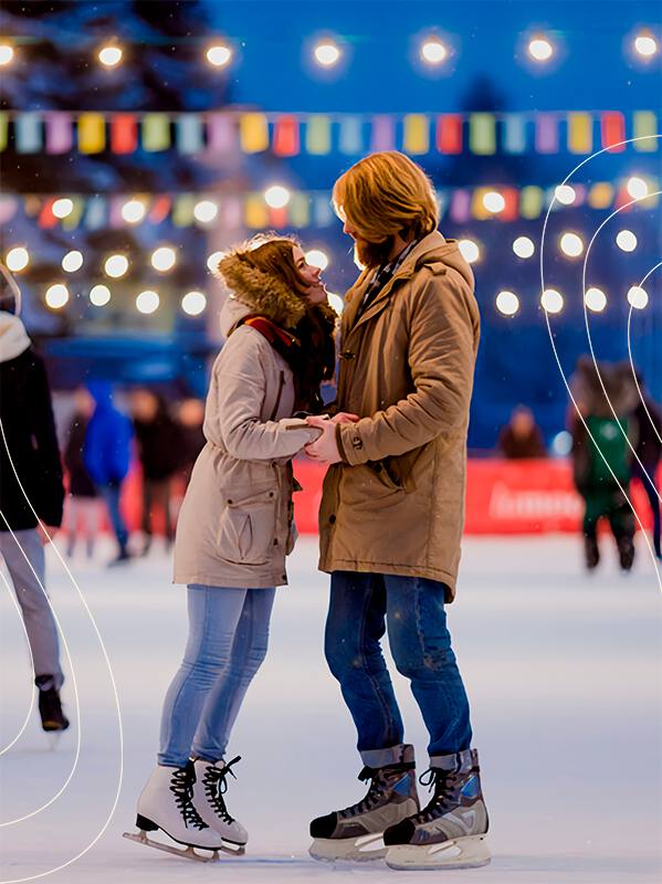 Пара катается на рождественском катке в Твери вечером: гирлянды, разноцветные огни и размытый праздничный городской фон.
