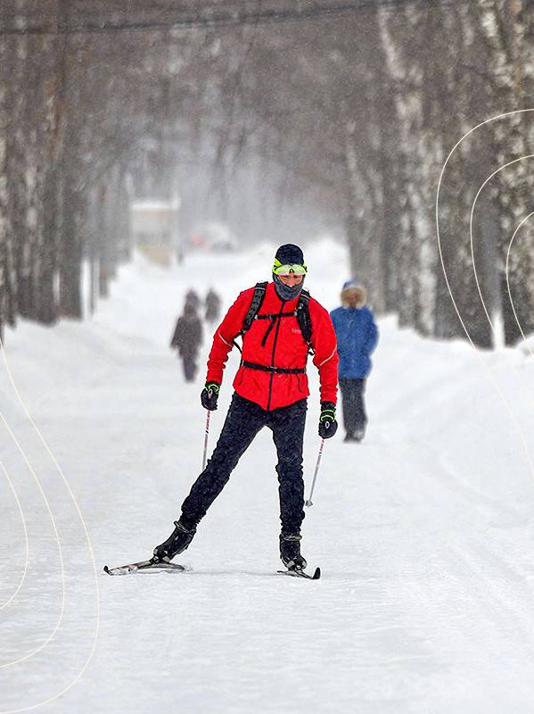 Лыжник пересекает заснеженный лесной маршрут рядом с Тверью: зимняя трасса среди деревьев, спокойная прогулочная сцена в снегопаде.