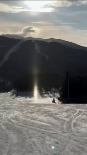 Короткий вертикальный кадр с сияющей колонной ледяных кристаллов на заснеженной равнине курорта, отражающей солнечный свет.