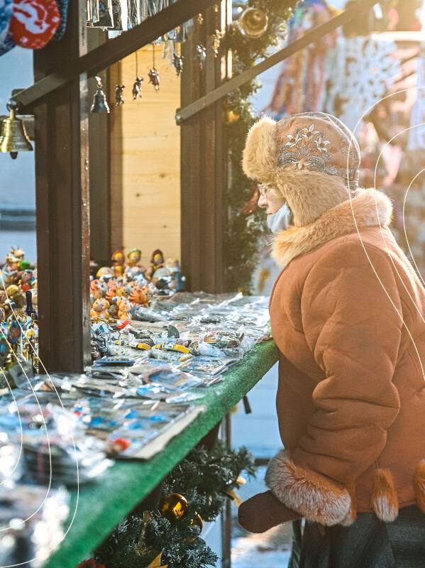 Ребёнок рассматривает сувениры на деревянной рождественской ярмарке в Твери: киоски с украшениями и праздничная витрина на улице.