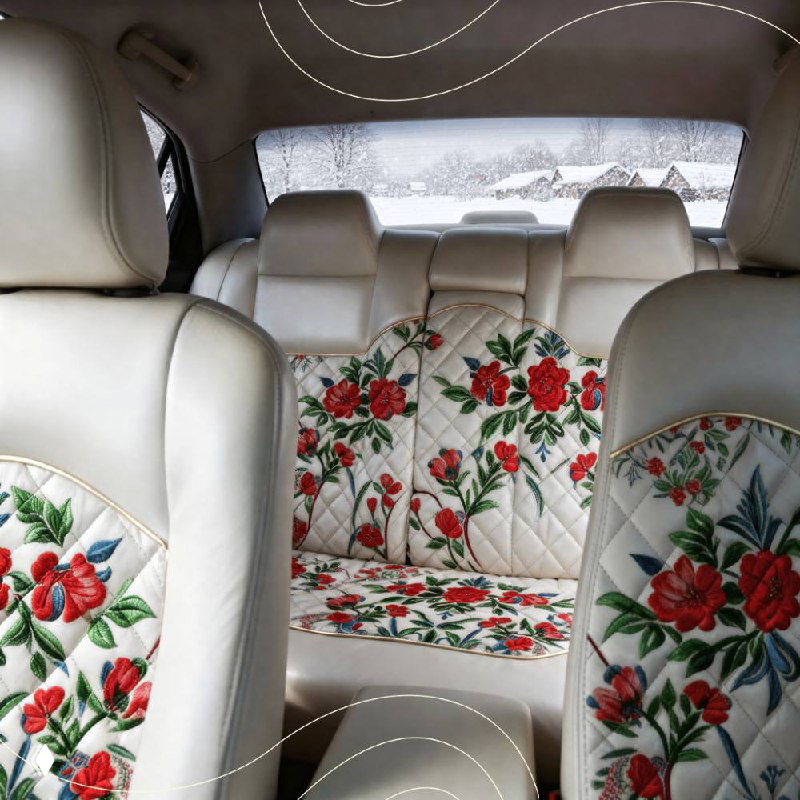 Задние сиденья автомобиля с декоративными накидками: светлый фон и яркие красные цветочные мотивы уральской росписи, вид из салона.