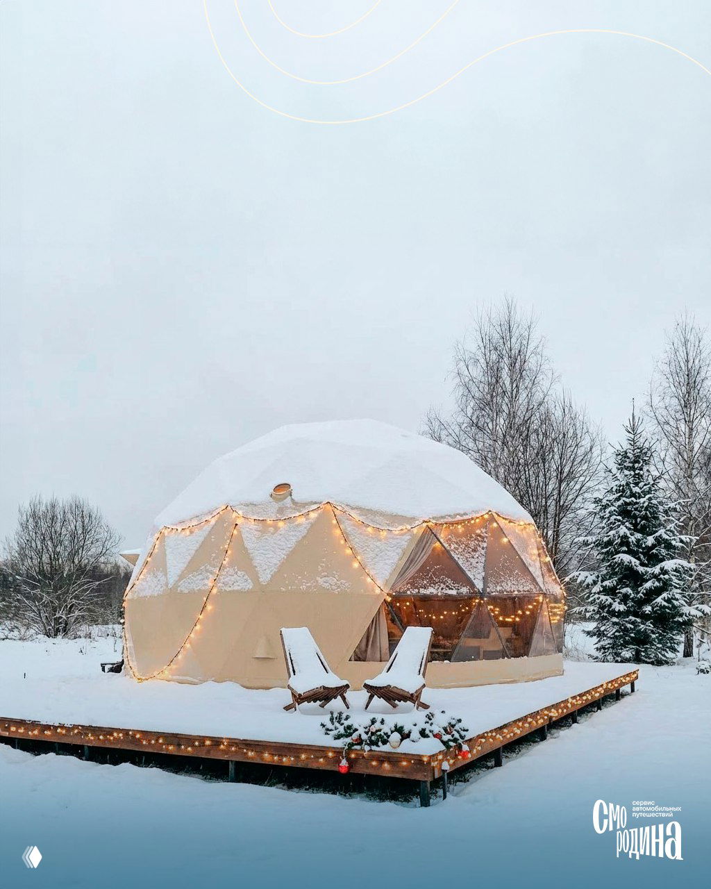 Геокупол на деревянной террасе, украшенный гирляндами и огнями, два шезлонга на снегу и огни в зимнем лесу позади.