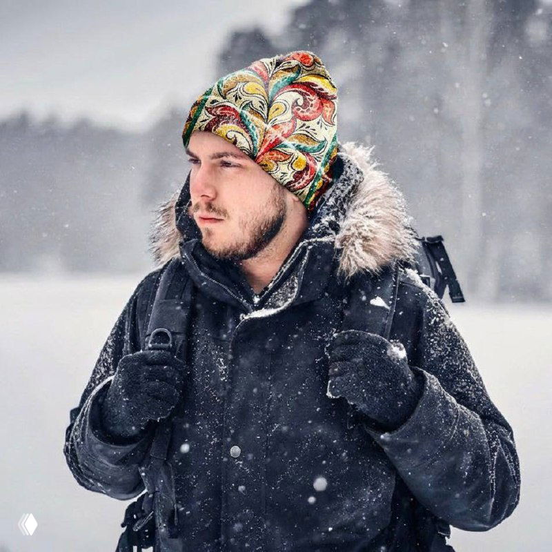 Мужчина в шапке с ярким ракульским рисунком стоит в заснеженном пейзаже — пример современной носки народного орнамента в одежде.