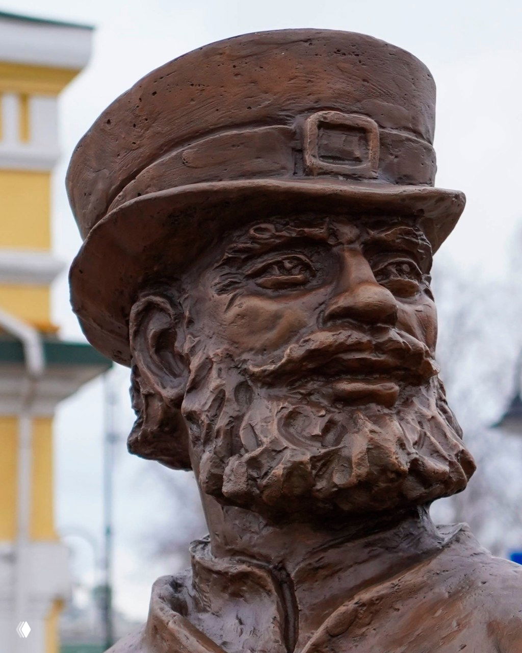 Крупный план головы бронзового ямщика в цилиндре — выразительная морщина и борода на скульптуре в городском пейзаже