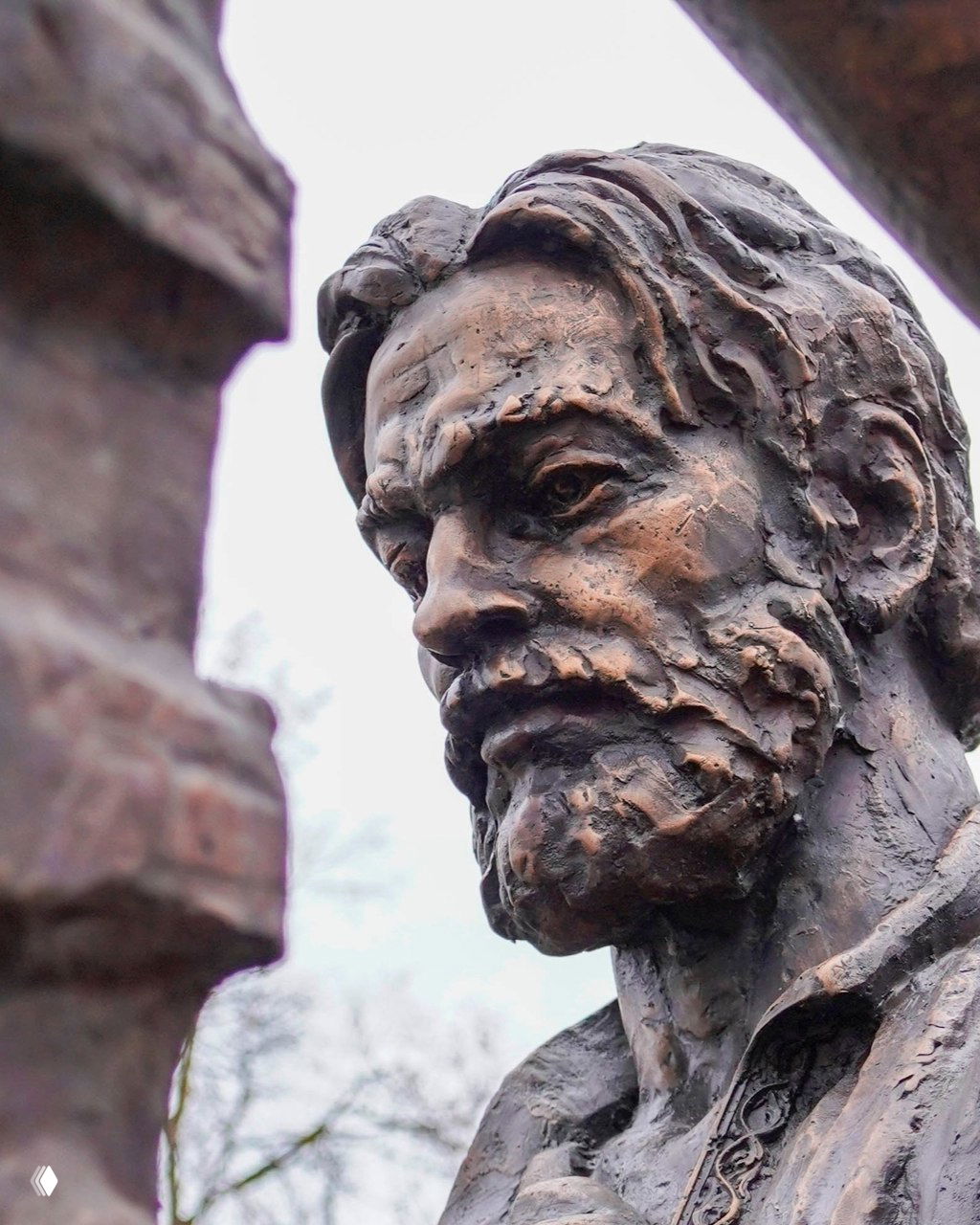 Крупный портретный вид бронзовой фигуры зодчего — выразительные черты лица и текстура поверхности на фоне зимних деревьев