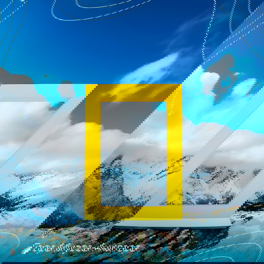 Жёлтая рамка на скалистом горном плато, внутри рамы видны заснеженные вершины и облака — изображение рамки у горы Мусса-Ачитара в Домбае.