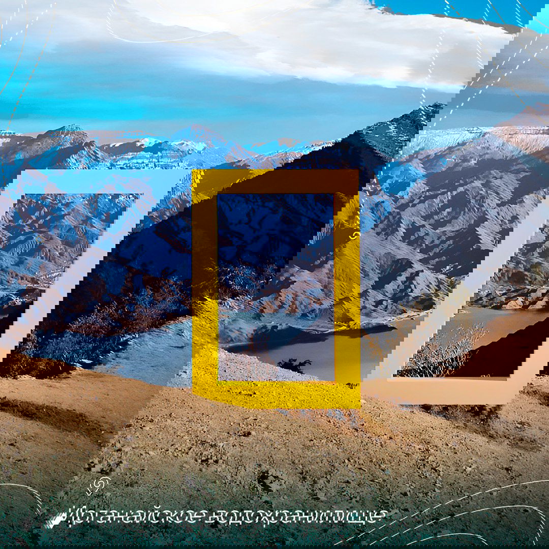 Жёлтая рамка установлена на фоне горной долины и водоёма, вдалеке видны террасы и берег — пейзаж, характерный для водохранилища в горах.